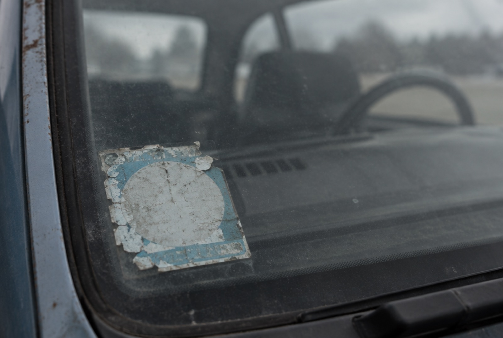 A faded, peeling inspection sticker in the corner of an old car's windscreen