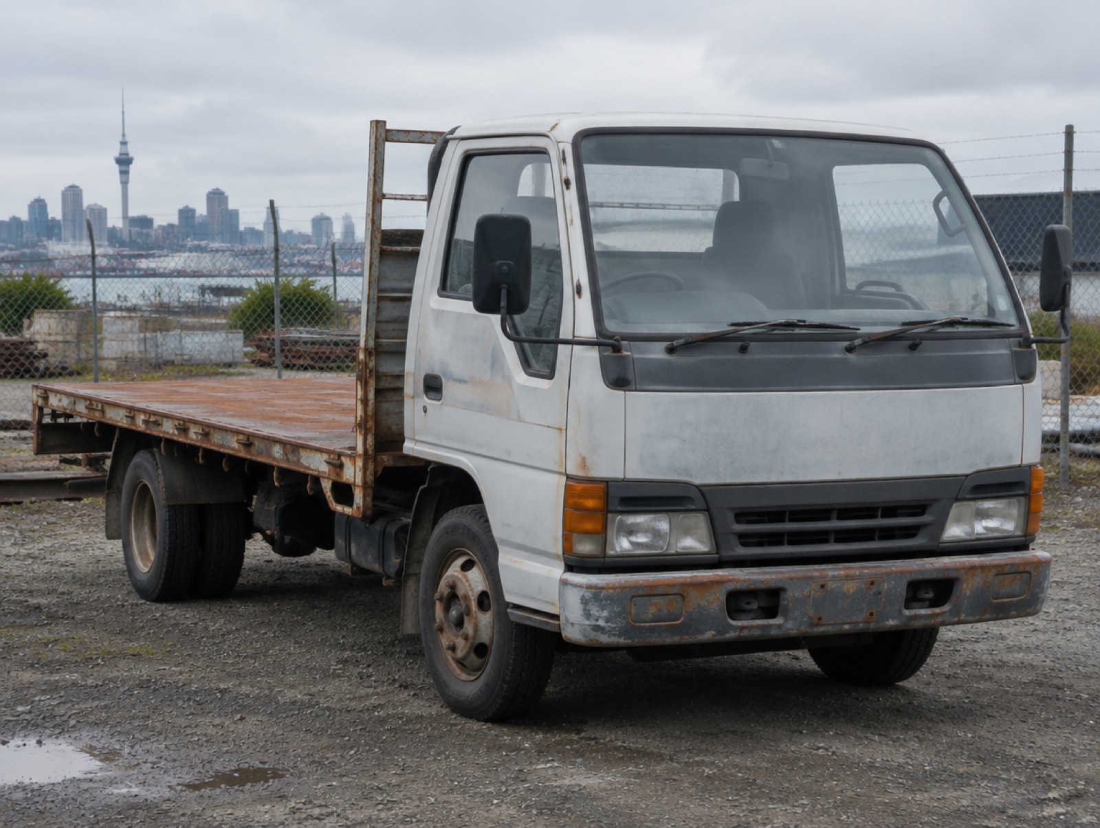 An older white light truck with a rusty flat deck in an industrial yard