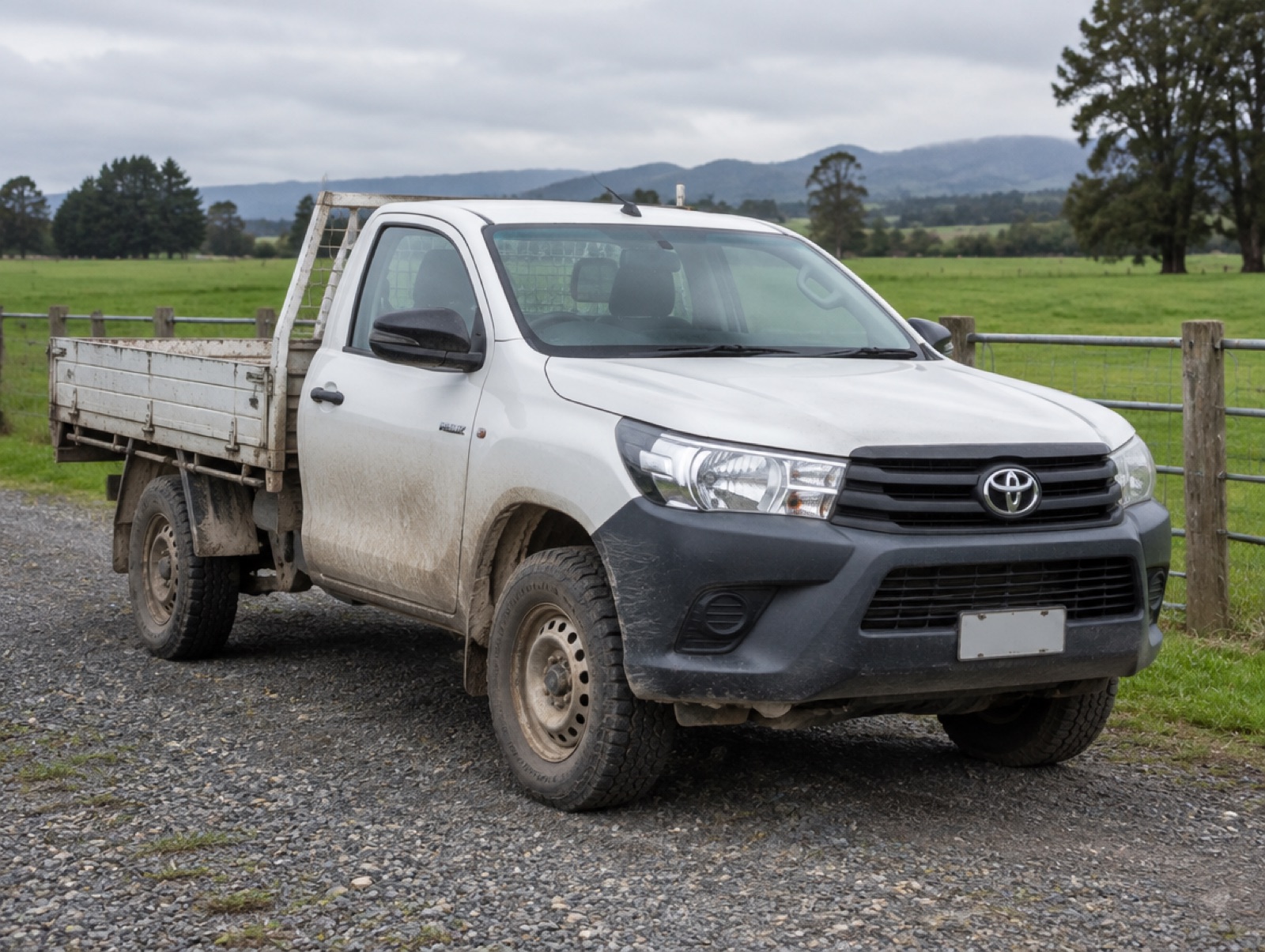 A well-used white ute with mud on the wheel arches on a gravel driveway