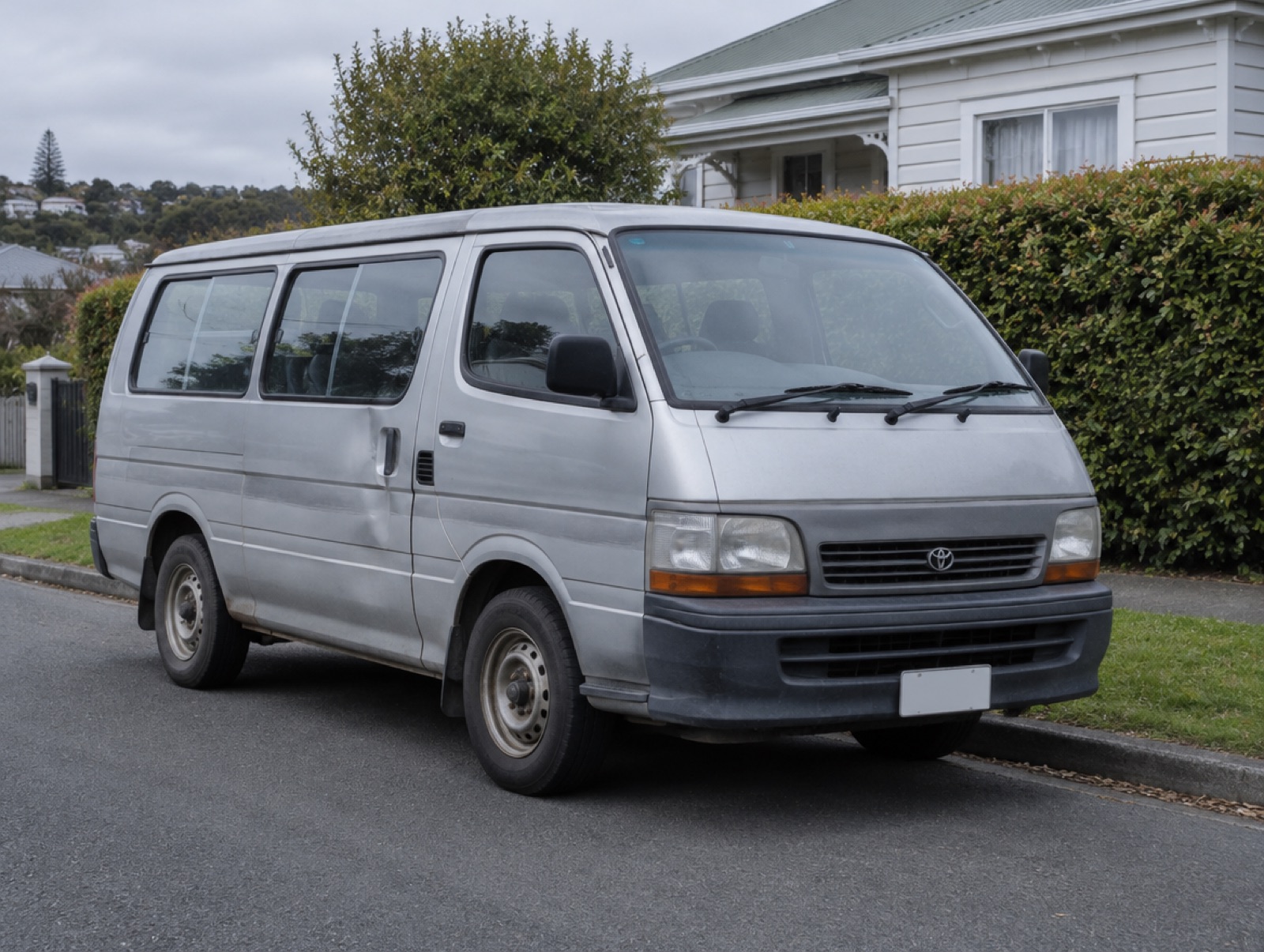 An older silver van with faded paint parked on a suburban street