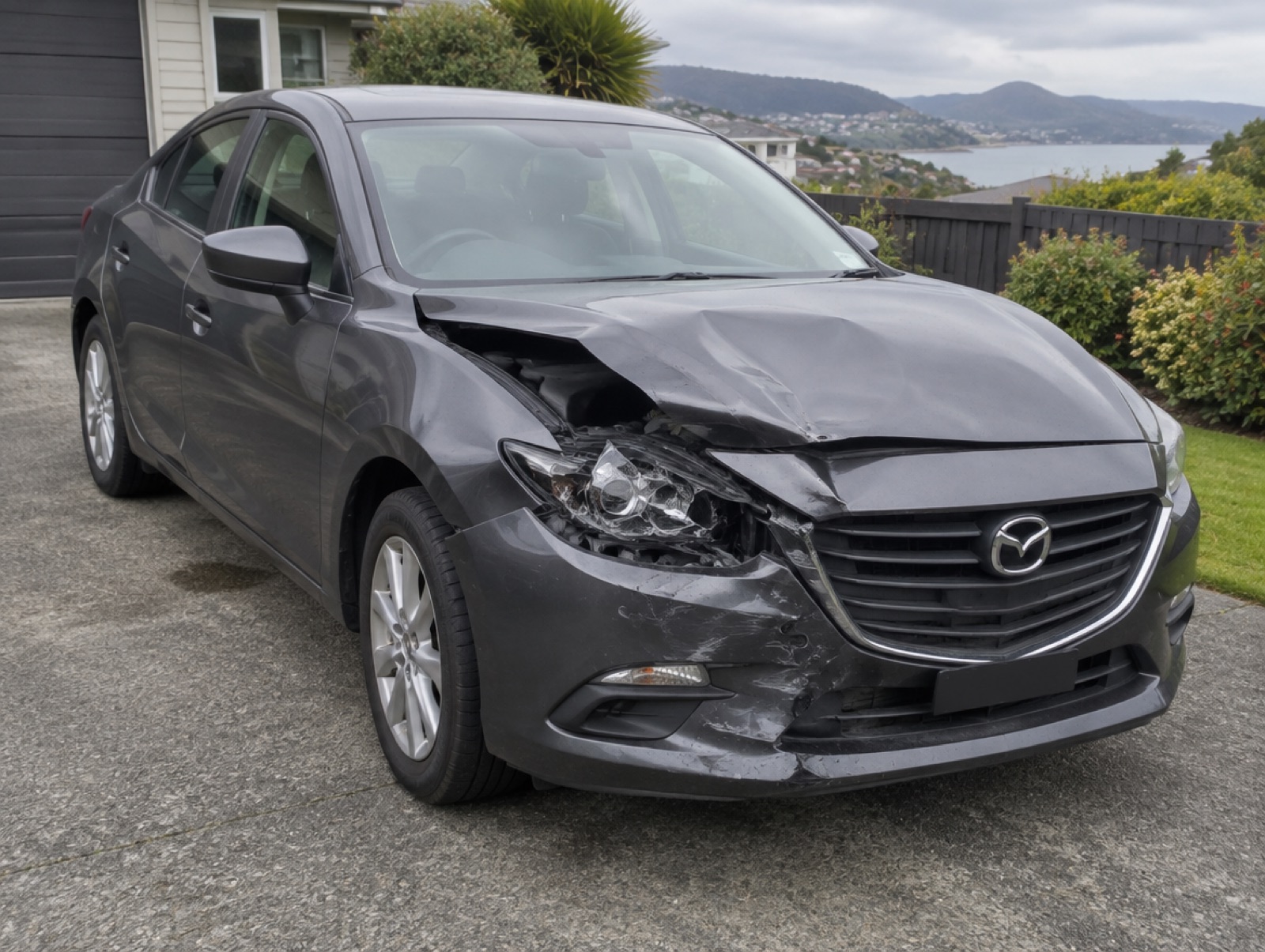 A grey sedan with a crumpled front end from a collision in a driveway